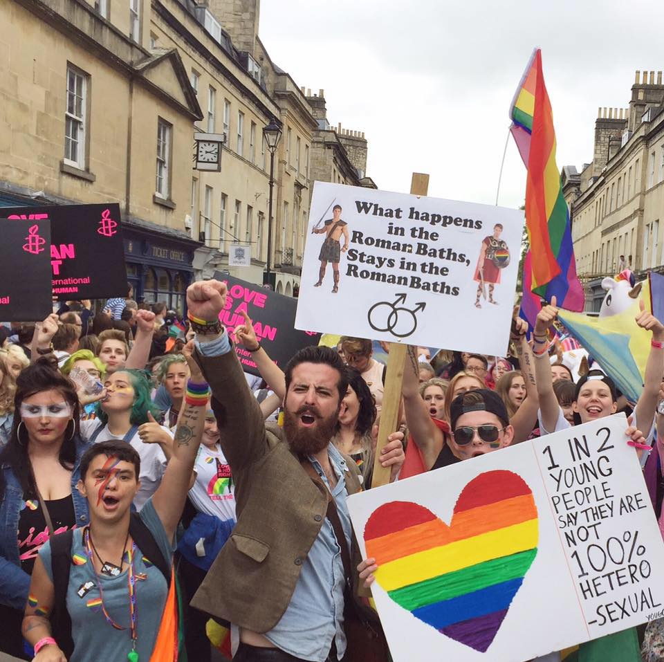 A group of protesters holding LGBT+ related signs in Bath