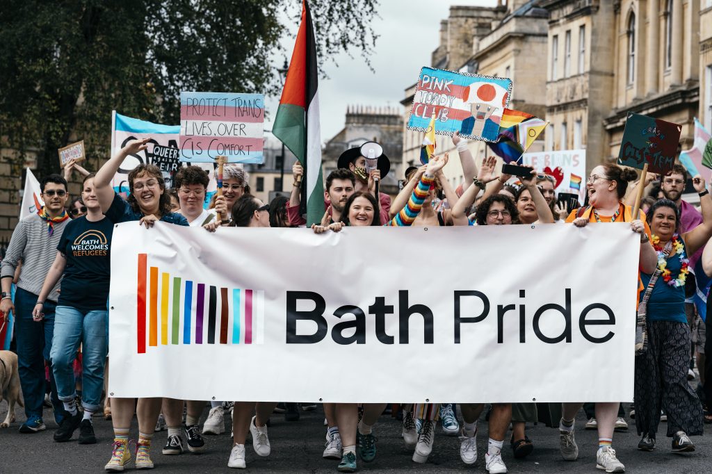 revellers at the front of the Bath Pride march 2025, holding a large banner and flags
