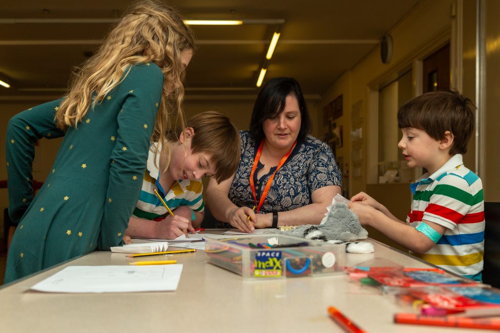 an adult with a group of three children drawing and doing crafts