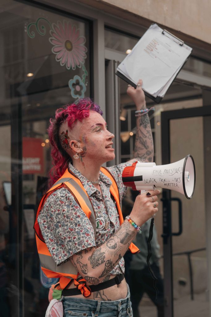 Nix leading the Bath Pride 2025 march holding a megaphone that reads "FREE PALESTINE" and "BLACK TRANS LIVES MATTER"