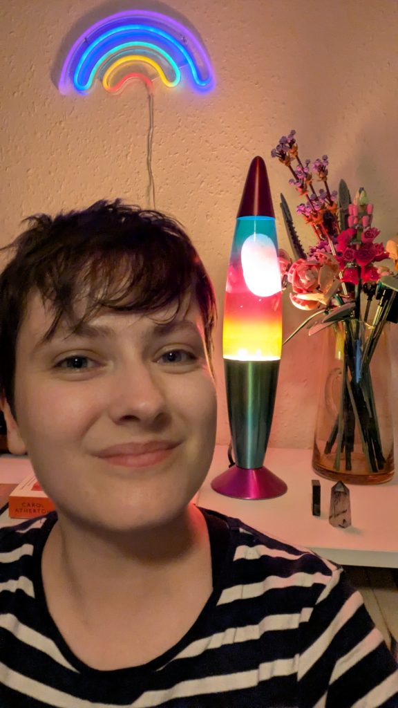 Lu in front of a rainbow light, a rainbow coloured lava lamp, and Lego flowers